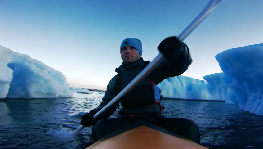 A dynamic shot of a kayaker navigating through icy waters dotted with icebergs. The camera follows the journey, highlighting adventure.