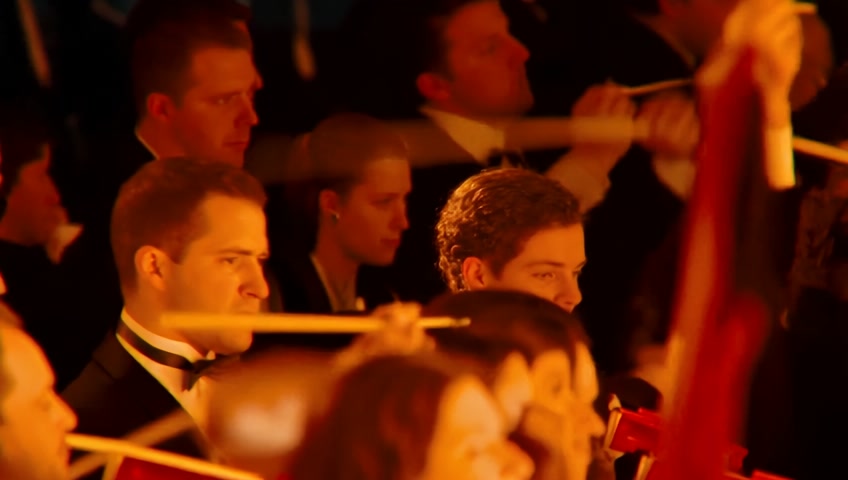 Orchestra in full motion, conductor energetic, cut to aerial shot of a huge Czech crowd singing in unison in a city square. Flags waving, slow-motion effect, golden light.