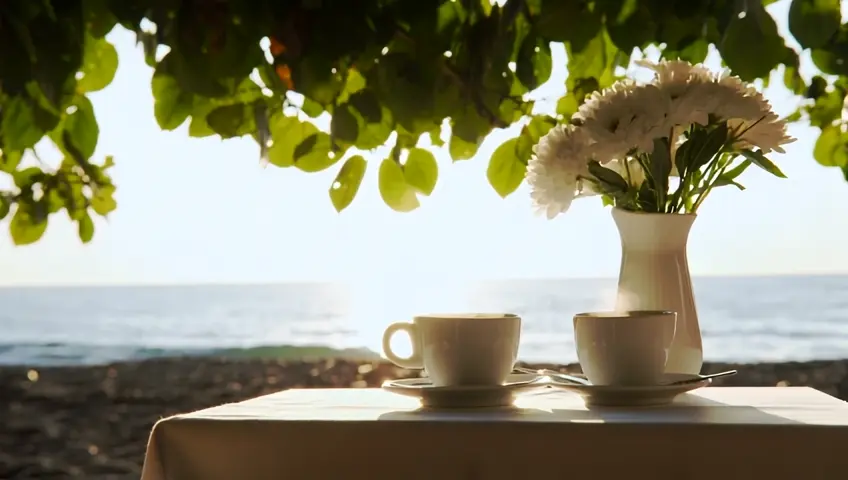 Create an image of a serene morning coffee scene with a warm sunrise filtering through lush green foliage near sea, highlighting a table set with two cups of steaming coffee and white flower bouquet in white vase, evoking a sense of peace and relaxation. Less
Magic Prompt  A serene morning coffee scene with a warm sunrise filtering through lush green foliage near the sea. There's a table set with two cups of steaming coffee and a white flower bouquet in a white vase. The scene evokes a sense of peace and relaxation. Less