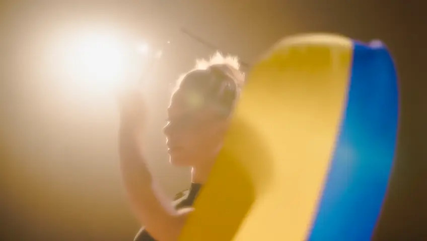 A slow-motion shot of a gymnast performing a ribbon routine, the ribbon creating colorful trails. The camera captures the elegance and flow of movement