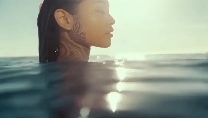 award winning closeup portrait photo of an polynesian woman, watergoddess, body tattoos, wading in the pacific ocean, partially submerged shot, style-moana, trending on artstation, highly detailed, fine detail, intricate, lens flare, backlighting, bloom.