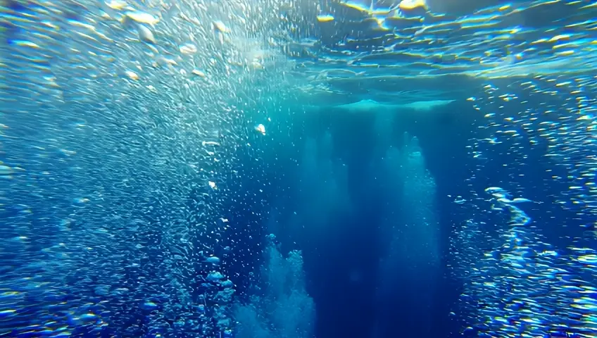 An underwater shot of bubbles rising to the surface in a deep blue sea. The camera follows the bubbles, creating a sense of depth and tranquility.