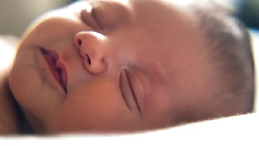 A close-up shot of a newborn baby's tiny hand gripping an adult's finger. The camera focuses on the contrast in size and the tenderness of the moment.