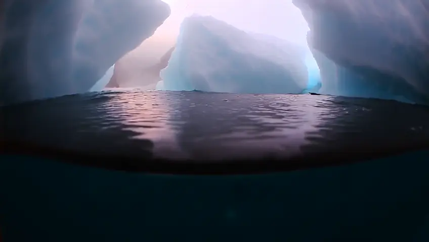 A panoramic underwater view of the Arctic Ocean floor, showcasing the haunting beauty of marine life and icy landscapes. Above the surface, colossal glaciers majestically collapse, sending rippling waves as they fragment into icebergs. The camera seamlessly pans 360°, capturing both the serene depths of the ocean and the dramatic transformation above, as water freezes upon contact with the Arctic chill, creating an otherworldly visual spectacle. The environment is illuminated by soft, refracted sunlight breaking through the ice, evoking a sense of awe and fragility of nature