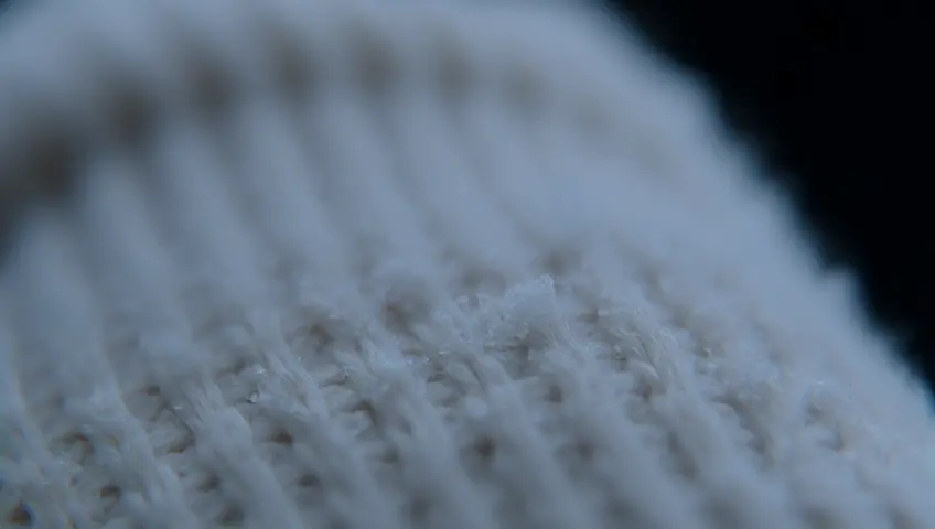 A close-up shot of a snowflake landing on a person's glove, revealing intricate patterns. The camera focuses on the delicate structure before it melts away.