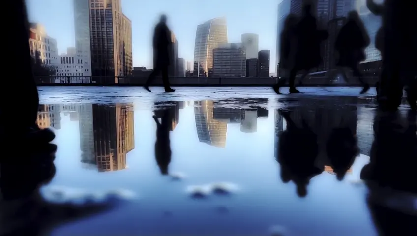 A dynamic shot of a cityscape reflected in puddles after rain, with people walking by. The camera captures reflections and the urban atmosphere