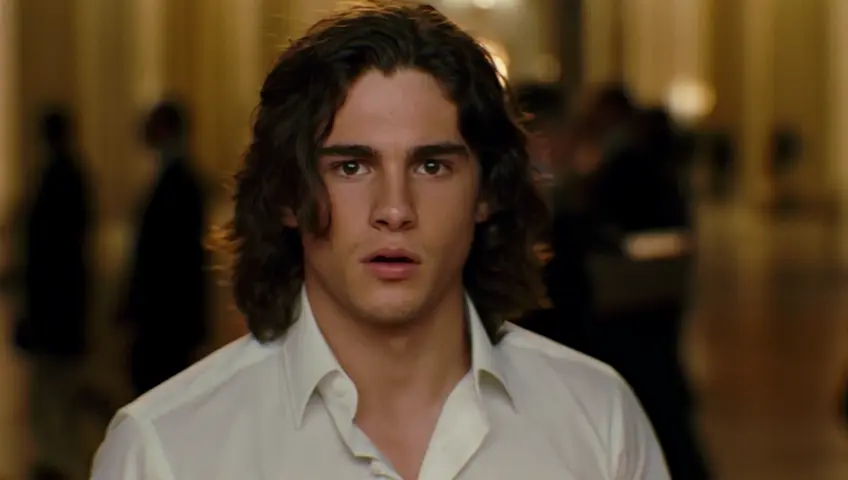 at night, inside the large building lobby, a surprised young man with Fringe long brown wavy hair in white short sleeve formal shirt standing at the lobby in front of crowd of people looking at the camera with surprised look on his face