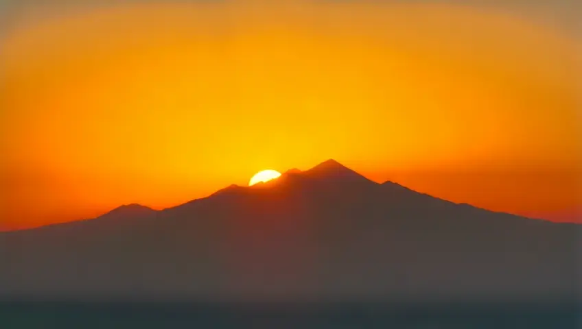 sun rising behind a mountain and rising into the sky. bright golden sky