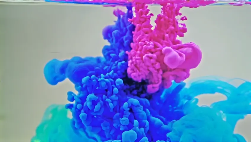 A slow-motion shot of ink droplets spreading in water, creating abstract patterns. The camera focuses on the fluid movement and merging colors