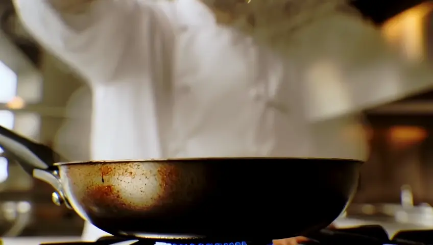 A slow-motion shot of a chef sprinkling spices over a sizzling dish in a kitchen. The camera captures the steam and aroma