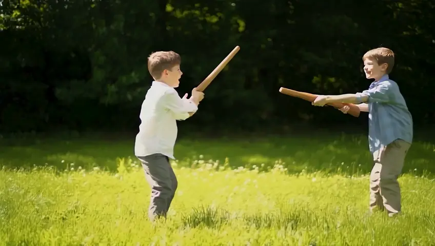 Little boys, 10 to 12 years old, are playing soldiers in a meadow at the edge of the forest. They have toy wooden machine guns in their hands