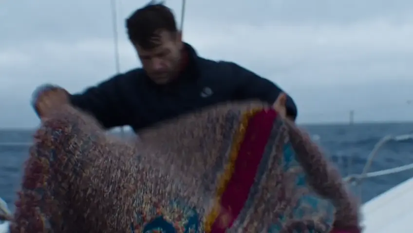 A sailor getting rolled up in a rug on a sailboat in rough oceans