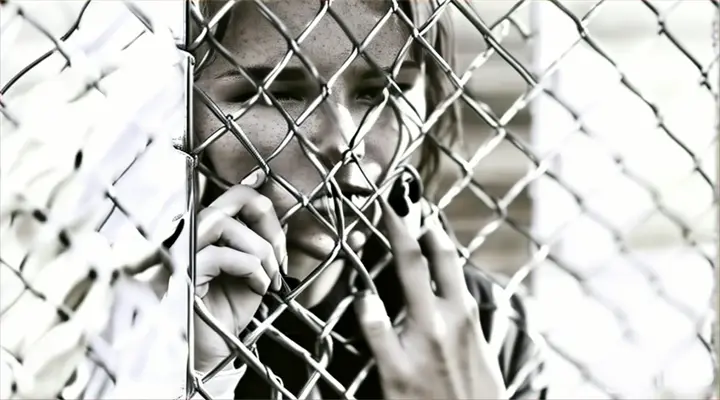 a woman leaning against a fence with her hand on the chain link fence
