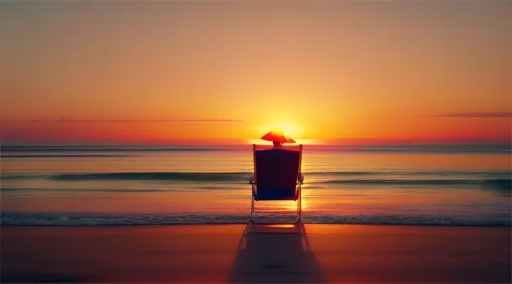 A person sitting in a simple beach chair silhouette against a brightly colored orange and yellow sunset sky over a calm ocean