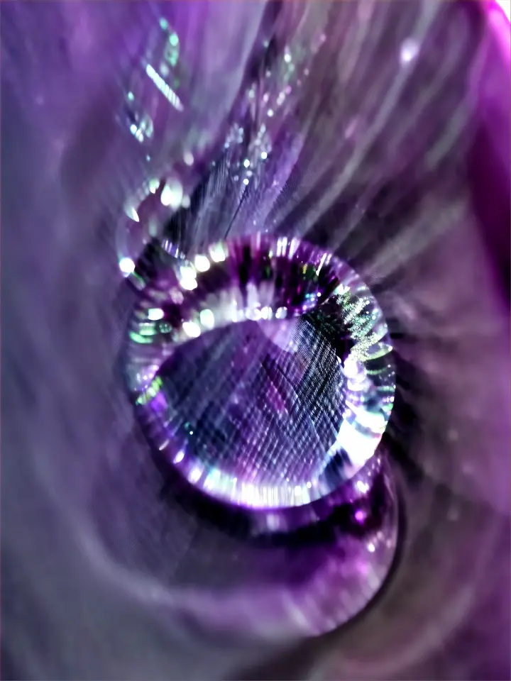 a close up of a water drop on a purple cloth. The light is going from right to left reflecting on the water drop.