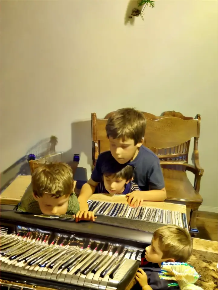 a boy and a boy sitting at a piano behind them are dinosaurs moving around