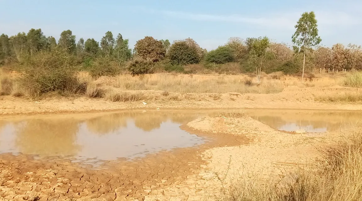 a body of water sitting in the middle of a dry grass field