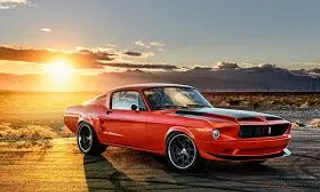 a red car parked on a road with the sun setting in the background