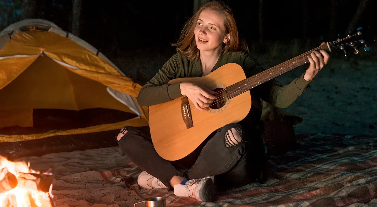 a woman playing a guitar in front of a campfire