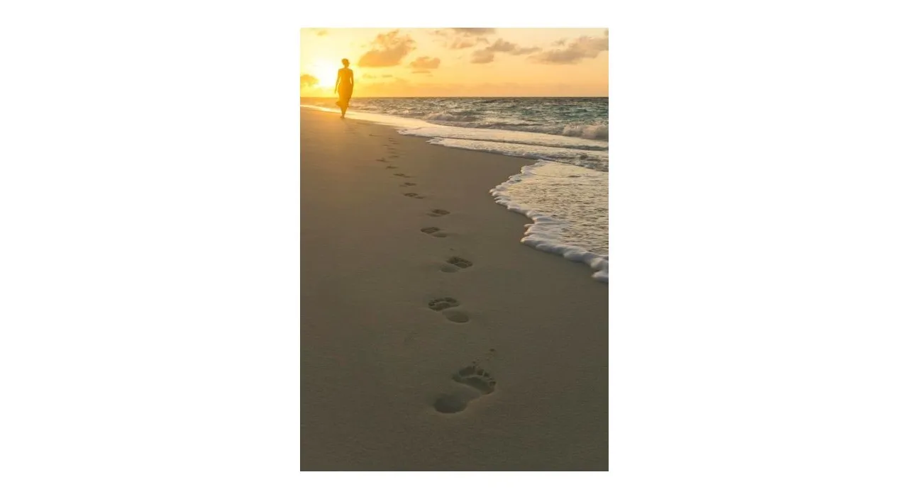 a woman walking along a beach with footprints in the sand