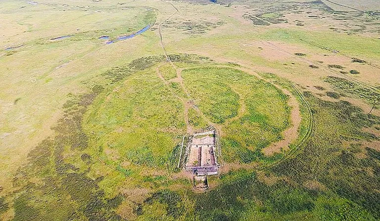 an aerial view of a grassy field with a building in the middle of it