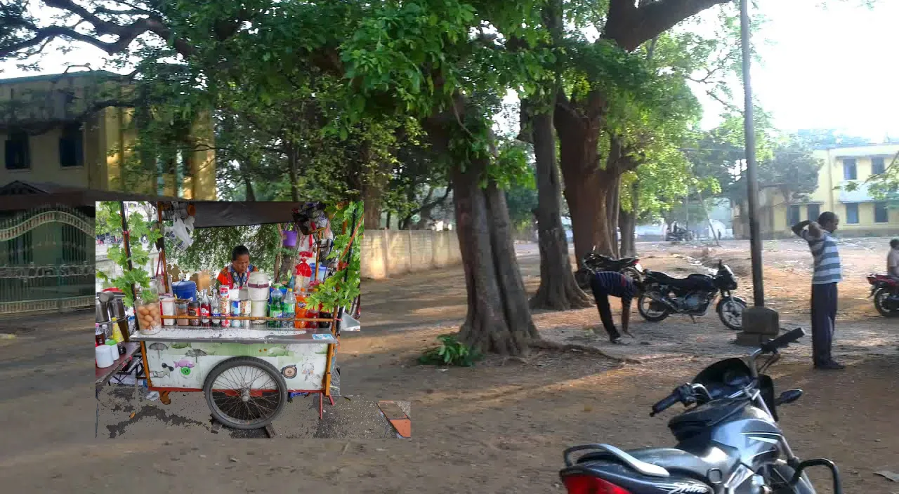 a motorcycle parked in front of a small cart and students are having tea and sitting under the tree