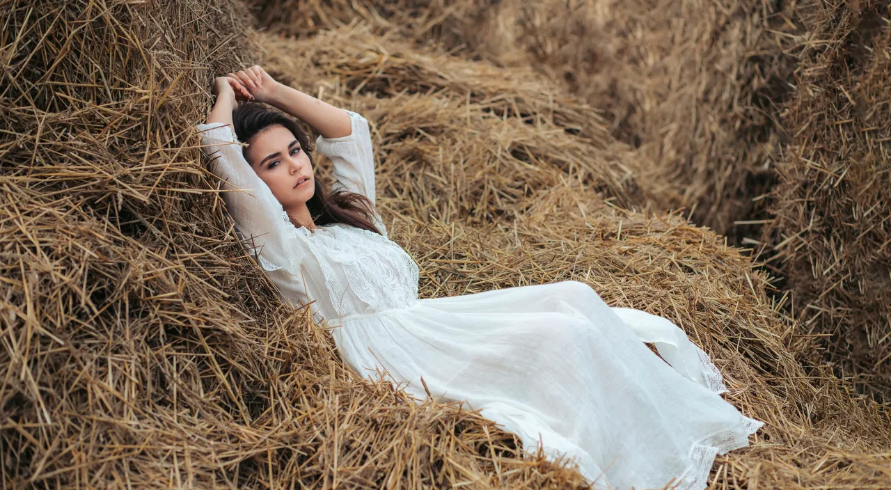 a woman in a white dress laying on a pile of hay