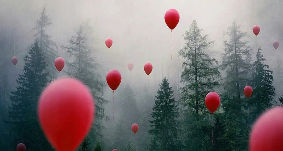 a group of red balloons flying over a forest