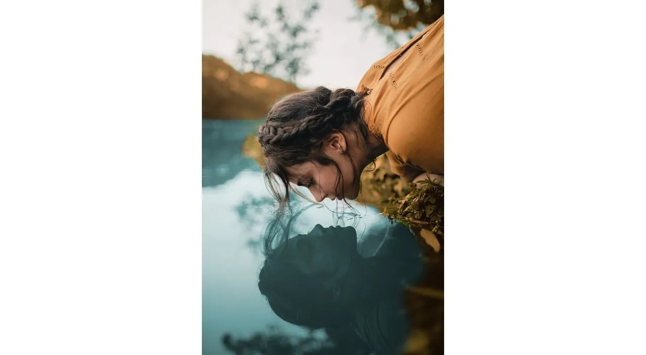 a woman looking at her reflection in the water