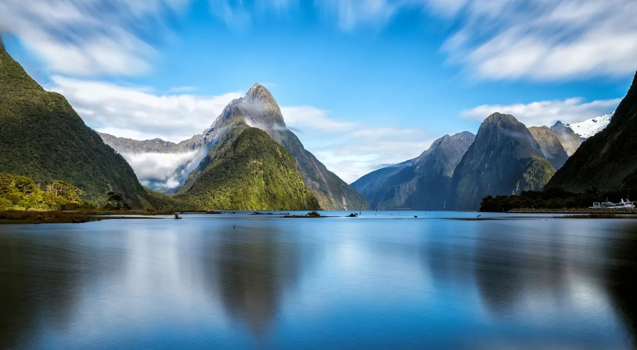 a lake surrounded by mountains under a cloudy blue sky