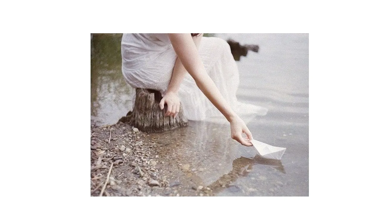 a woman in a white dress reaching for a paper boat