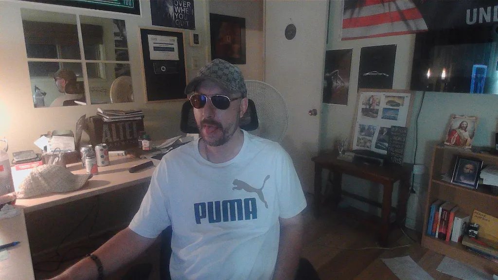 a man sitting in a chair wearing a white shirt who make business on is computer, gucci cap and sunglasses