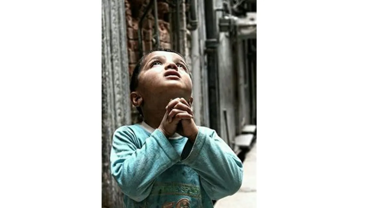 a young boy standing in front of a building praying