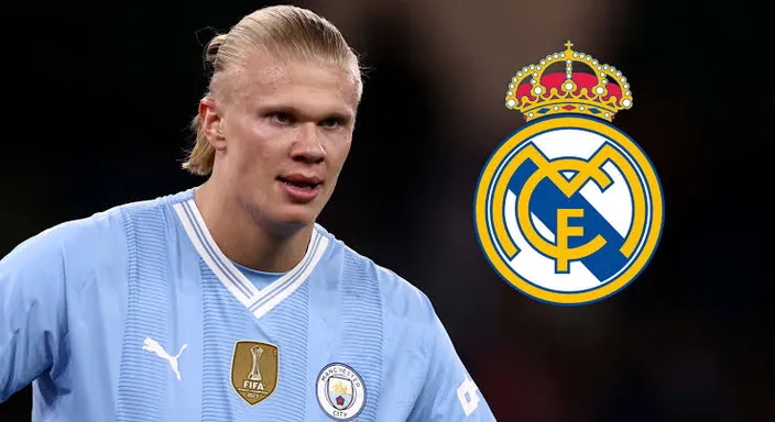 Erling haaland in a blue uniform standing in front of a real madrid logo