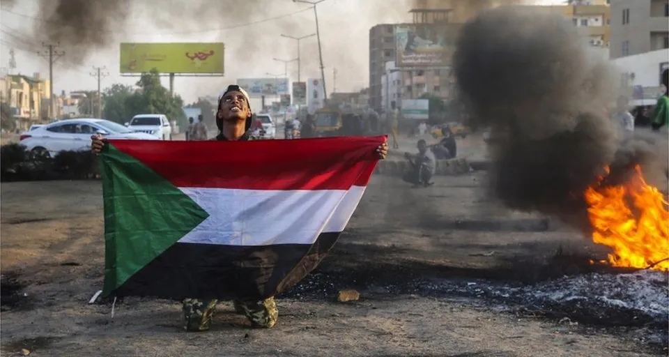 a person holding a flag of sudan in front of a fire