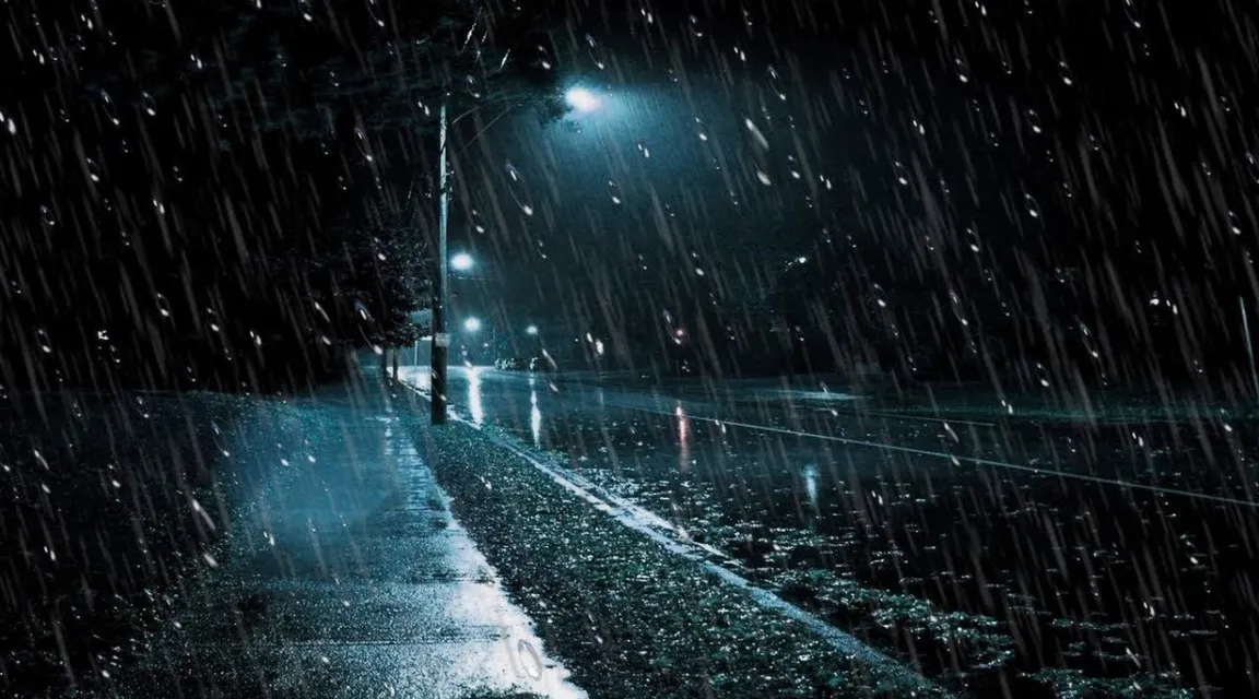 Rain drops on a window with streetlights reflecting in the water, a cozy interior in the background