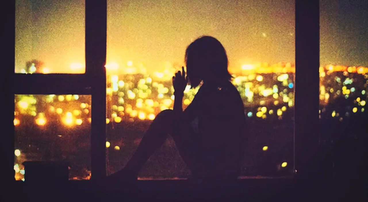 a person sitting on a window sill looking out at a city at night