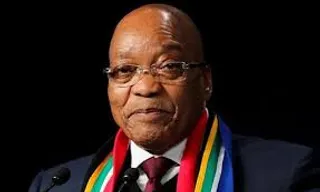 president zuma , in a suit and tie with a colorful scarf showing south african colors around his neck