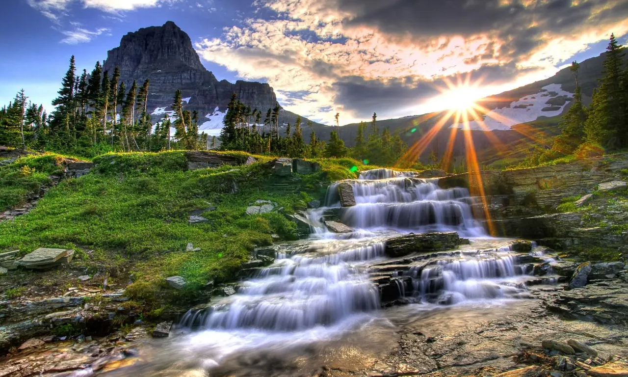 the sun is shining over a waterfall in the mountains