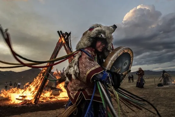 a man in a costume holding a drum in front of a fire