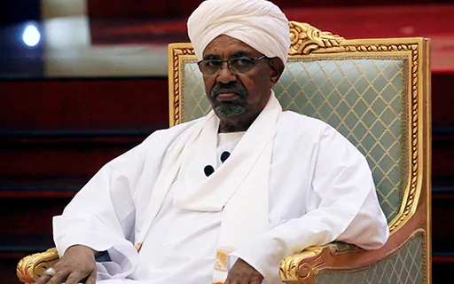 a man in a turban sitting in a chair, raising his hand