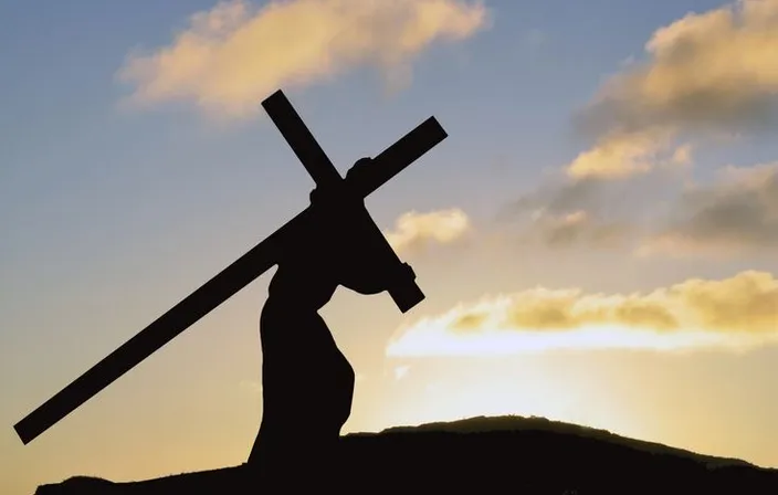 a silhouette of a person carrying a cross