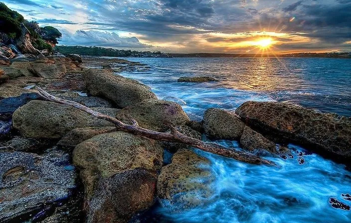 a sunset over a body of water with rocks in the foreground