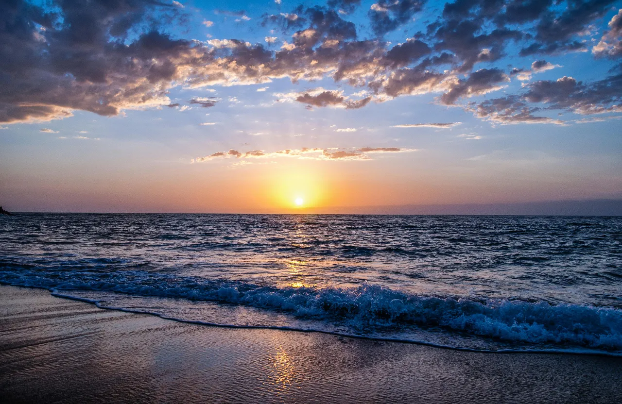 the sun is setting over the ocean on the beach