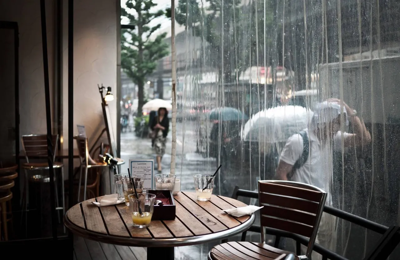 A person capturing a rain-soaked table with a cheerful umbrella backdrop and bright, reflective puddles