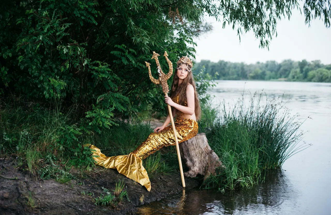 a woman in a mermaid costume sitting on a rock next to a body of water