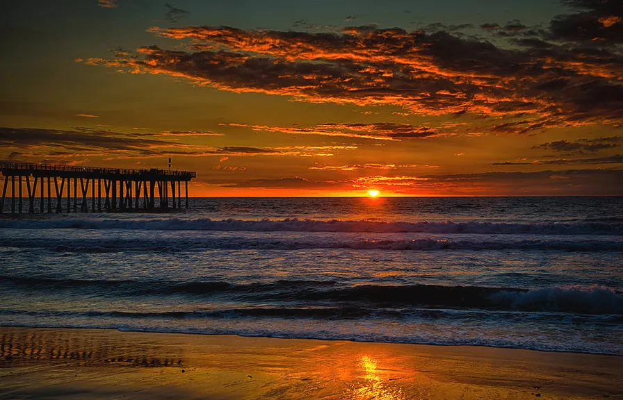 a sunset over the ocean with a pier in the distance