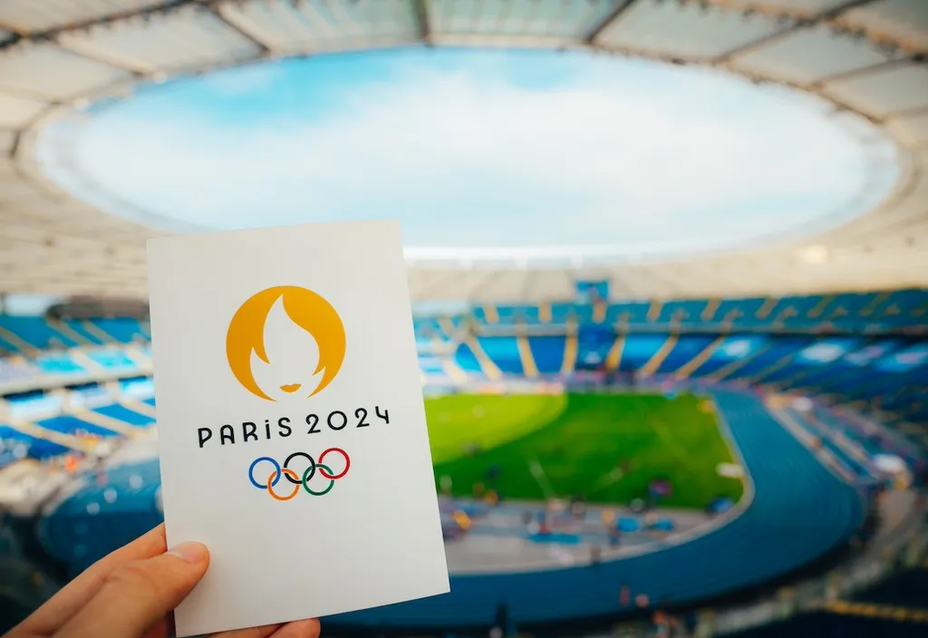 a hand holding a piece of paper of OLYMPICS 2024 in front of a stadium