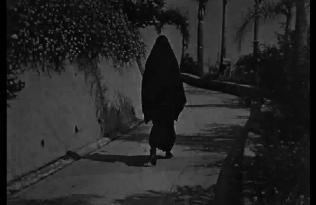 a woman walking down a sidewalk next to a tree