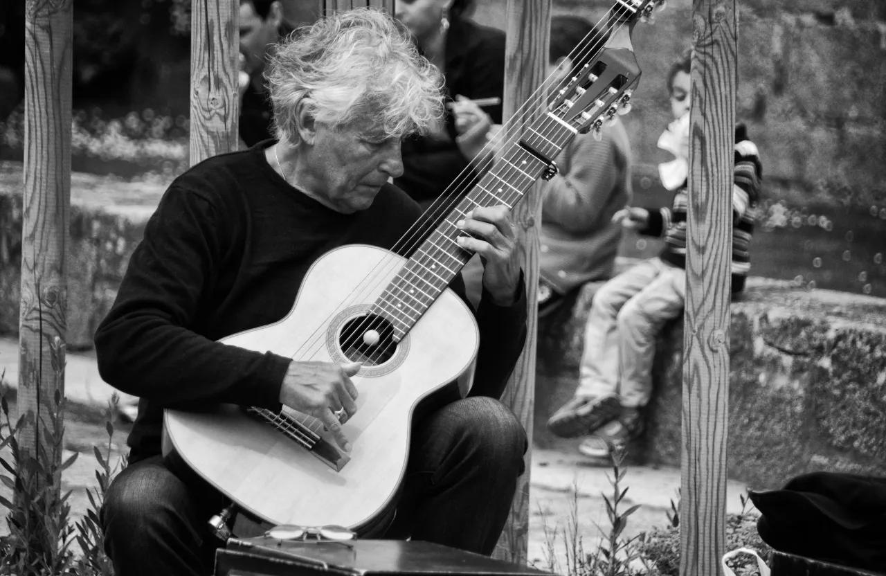 a old man sitting on a bench playing a black guitar